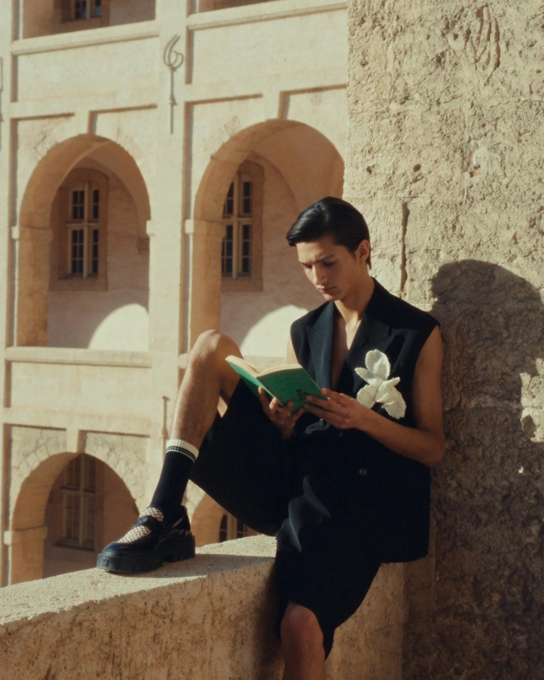 Jeune homme lisant sur un balcon ensoleillé entouré d'architecture historique, photographié par l'agence créative PAF PAF à Marseille pour AMIRI – moment de détente et d'élégance.